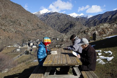 Tres persones llegint davant de l'ermita Sant Quirc d'Alins, amb el poble al fons (Foto: ACN/Marta Lluvich)