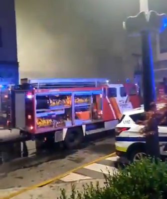 Un camió de Bombers i un cotxe de la Policia, aquesta matinada davant el Centre Cultural i de Congressos Lauredià, cobert de fum per l'incendi (Imatge: Comú de Sant Julià de Lòria)